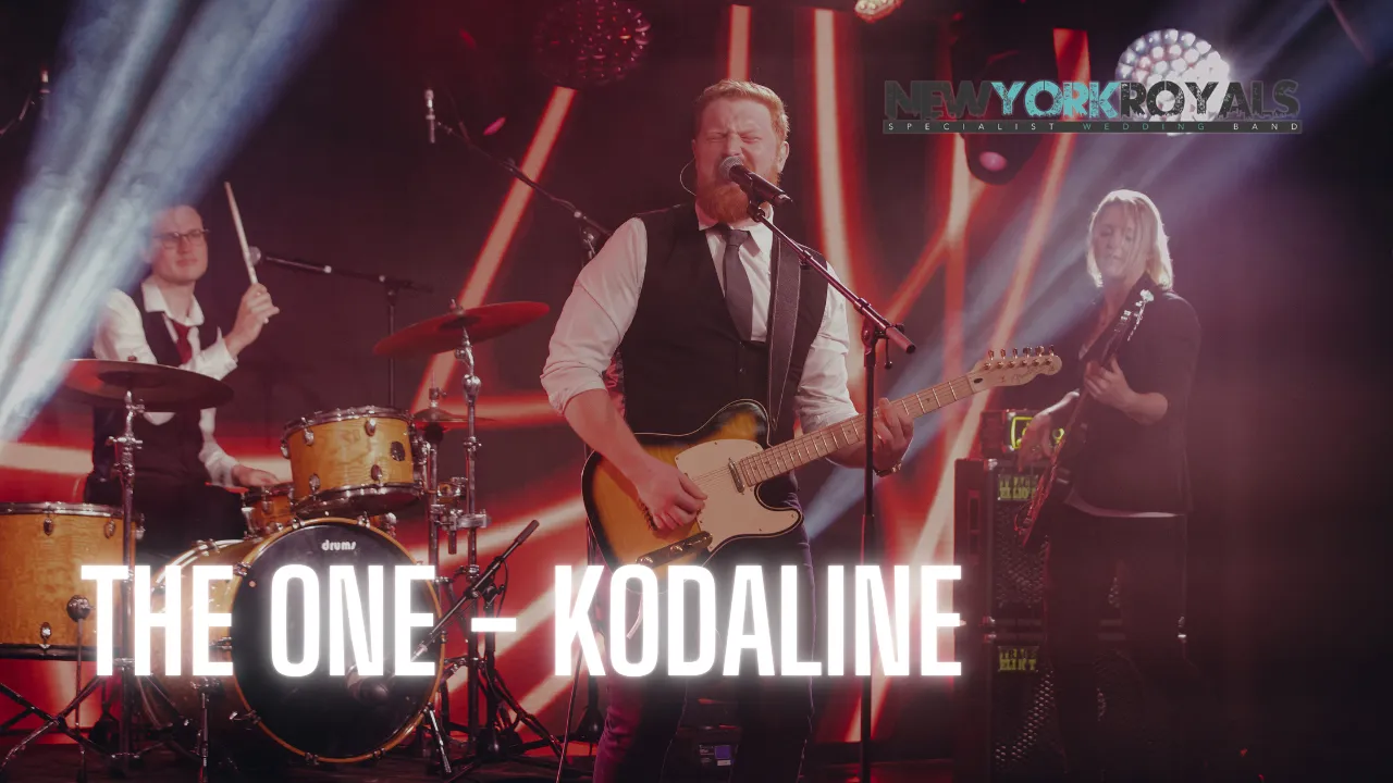 Musician playing guitar on stage with red stage lighting and text THE ONE - KODALINE
