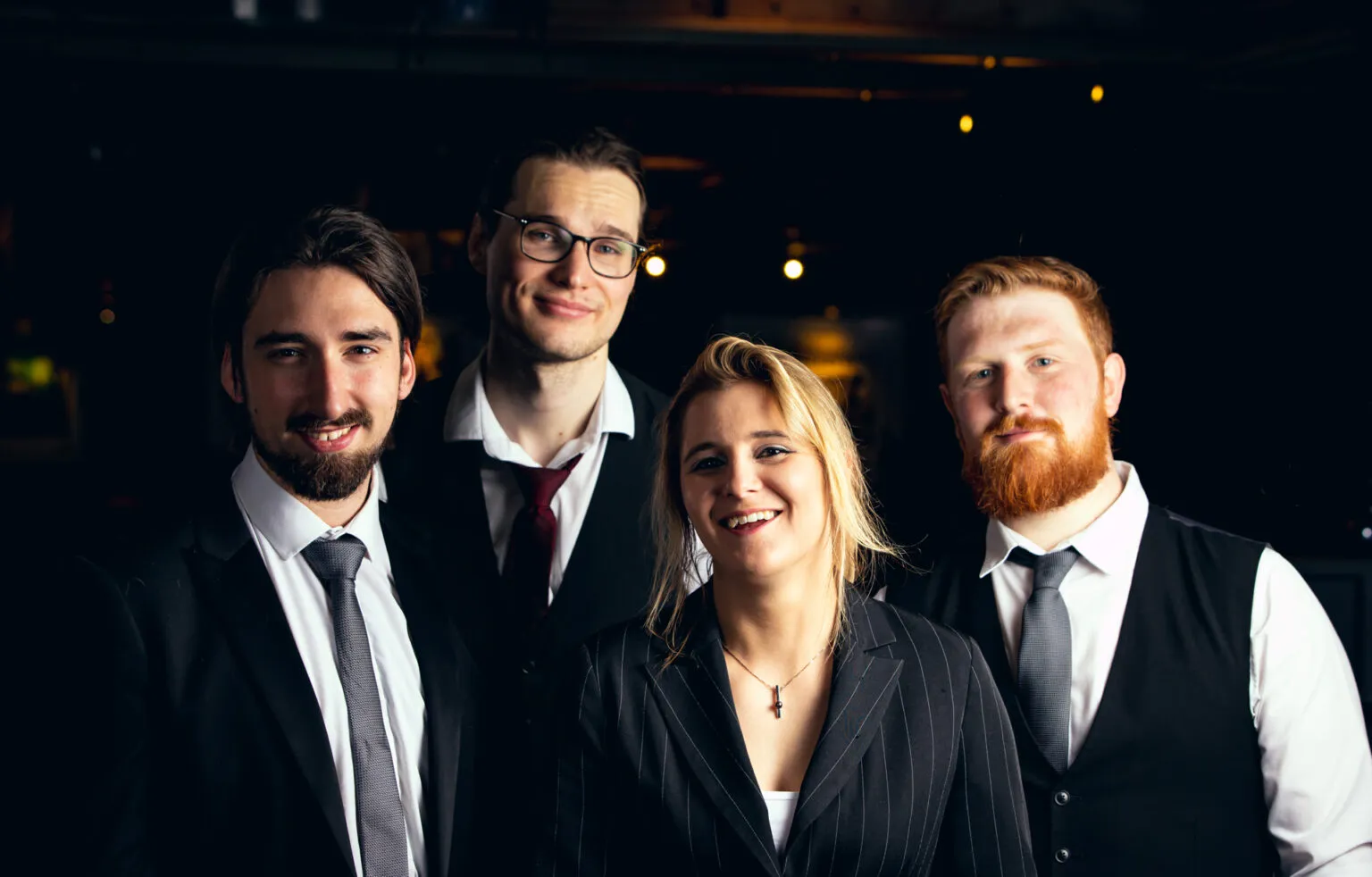 Four young professionals dressed formally smiling against a dark background.